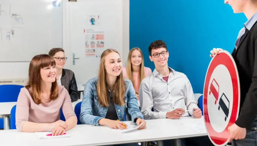 Insegnante mostra un segnale stradale a studenti sorridenti. Si può guidare di notte con il foglio rosa A1?