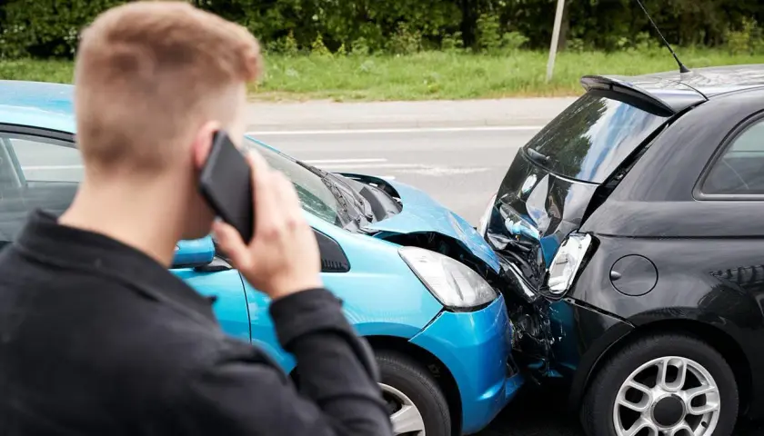 Uomo al telefono dopo un incidente. Le auto sono danneggiate, un sinistro che richiederà un **scoperto assicurativo**.