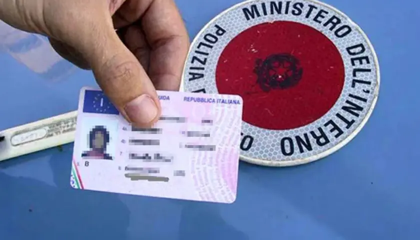 Patente italiana in mano, accanto a un disco di Polizia Stradale. Guida sicura per sapere come recuperare i punti della patente.