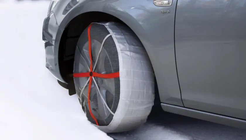 Auto grigia su neve con calze da neve omologate montate su una ruota. Sicurezza invernale garantita.
