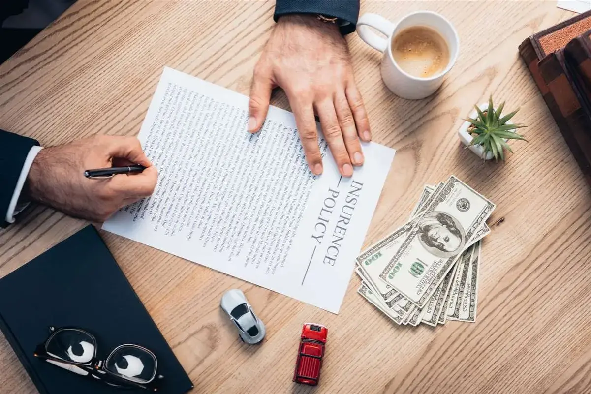 Firma un contratto di assicurazione senza franchigia: cosa significa? Pagamento in contanti, auto e caffè sul tavolo.