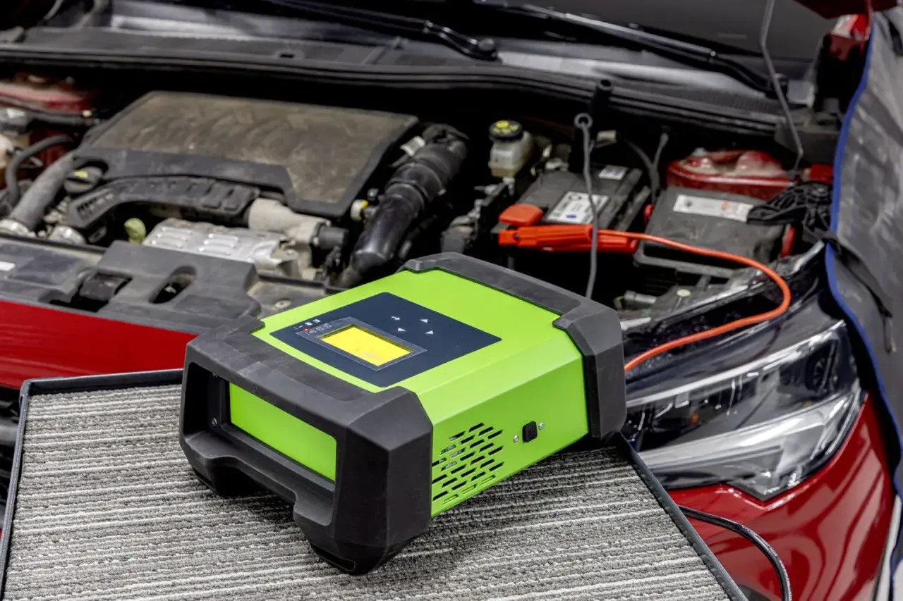 Carrozzeria rossa con cofano aperto, motore e batteria. Un caricabatterie verde è collegato per risolvere la batteria scarica.