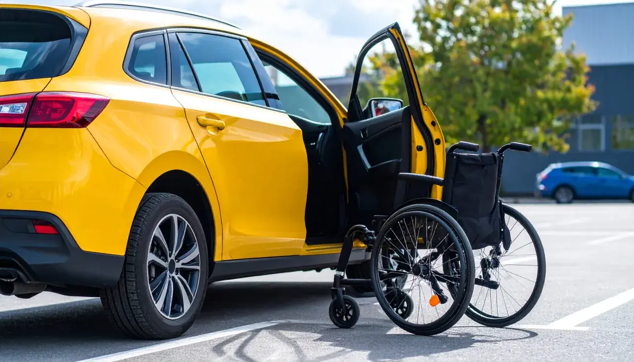 Auto gialla con portiera aperta e carrozzina accanto, simbolo di un nuovo inizio e del passaggio di proprietà auto acquistata con legge 104.