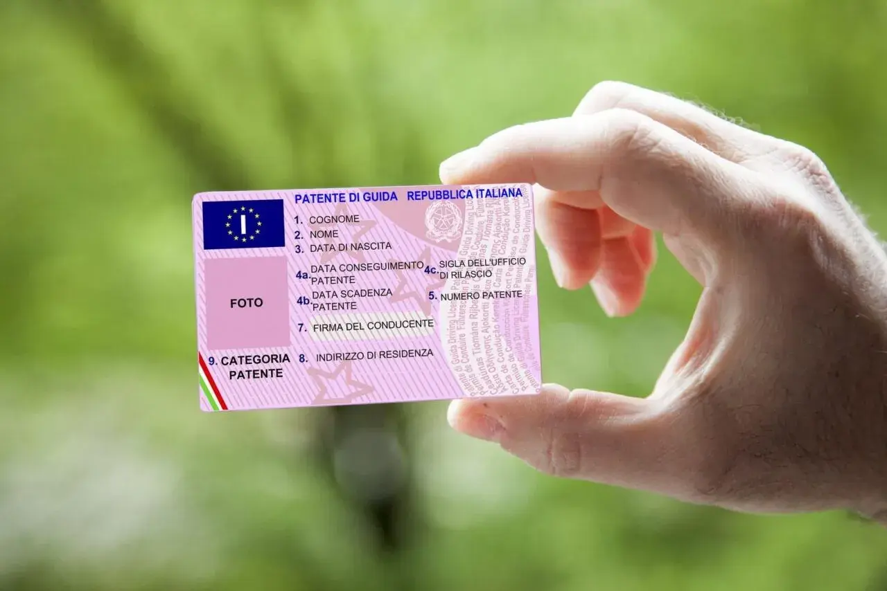 Mano che mostra una patente di guida italiana. Il numero di patente è visibile, con il codice patente 71 che indica la categoria.
