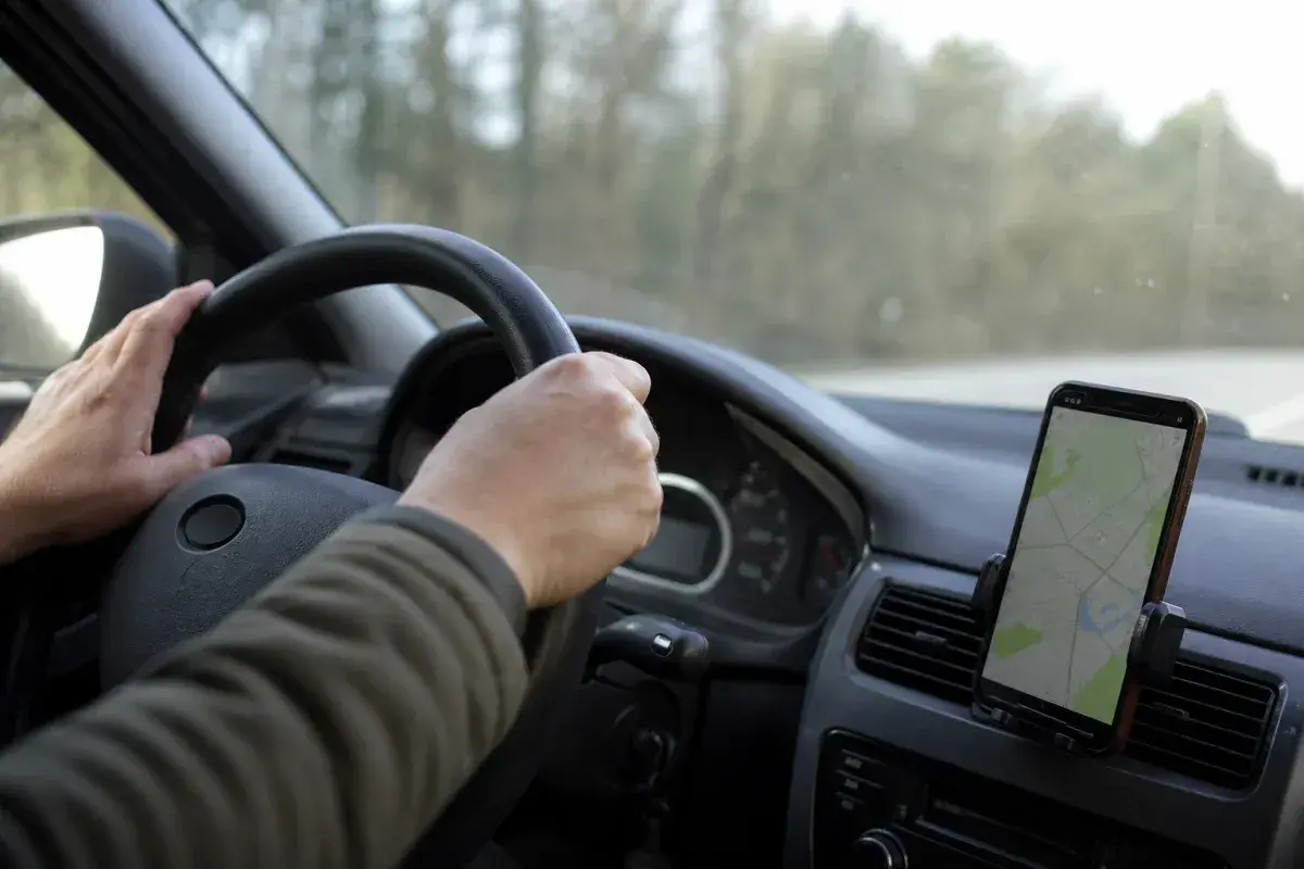 Mani sul volante, un cellulare con mappa mostra la strada. La guida con cellulare è essenziale per orientarsi.