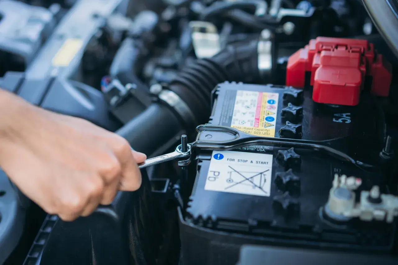 Mano con chiave inglese che allenta il bullone per staccare la batteria auto e non farla scaricare.