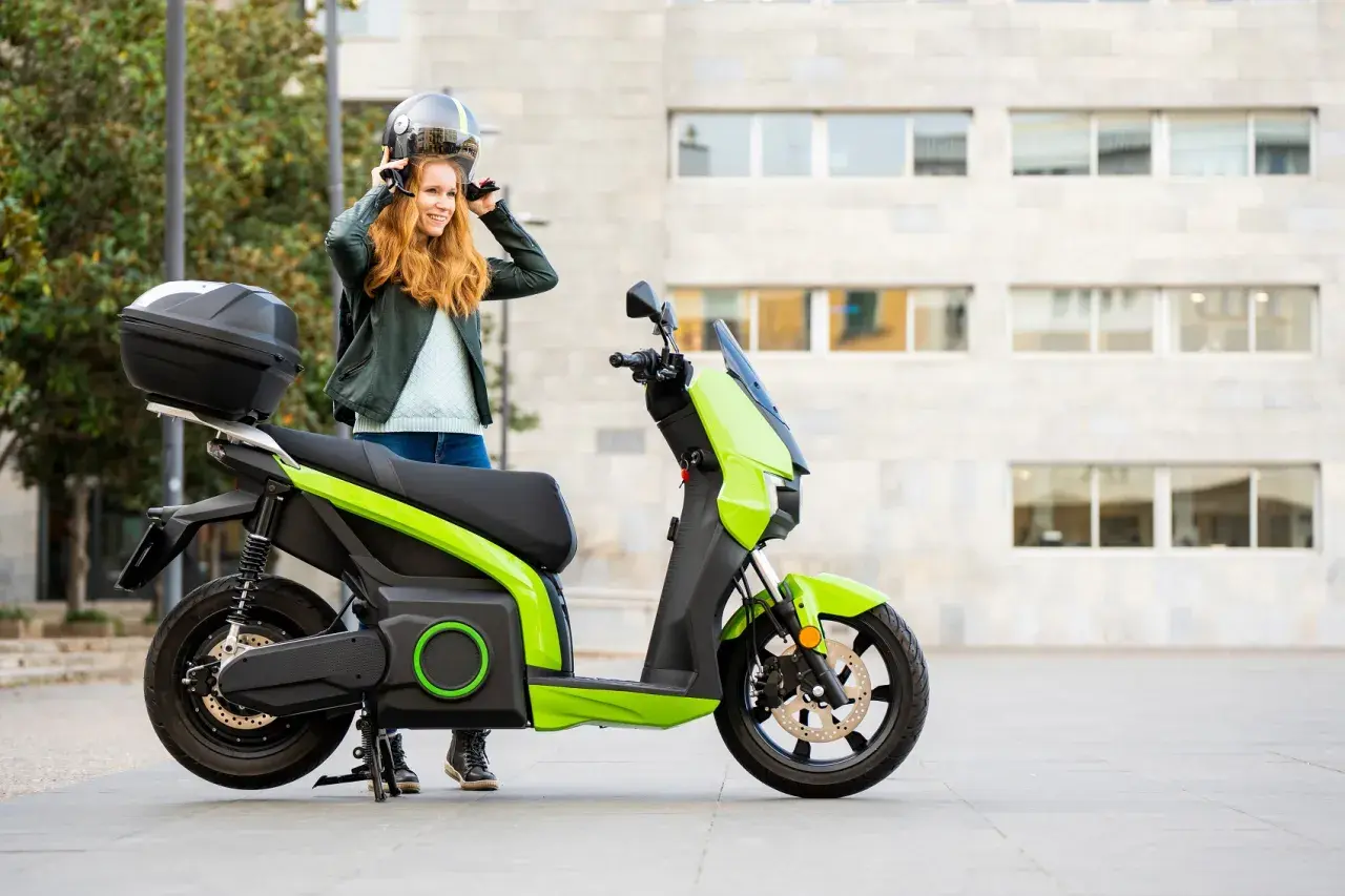 Donna sorridente mette il casco accanto al suo scooter elettrico verde brillante.