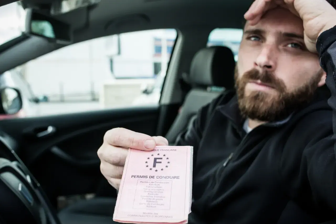Uomo sconsolato in auto mostra la patente, forse a causa di una infrazione per eccesso di velocità che ha portato alla sospensione patente velocità.