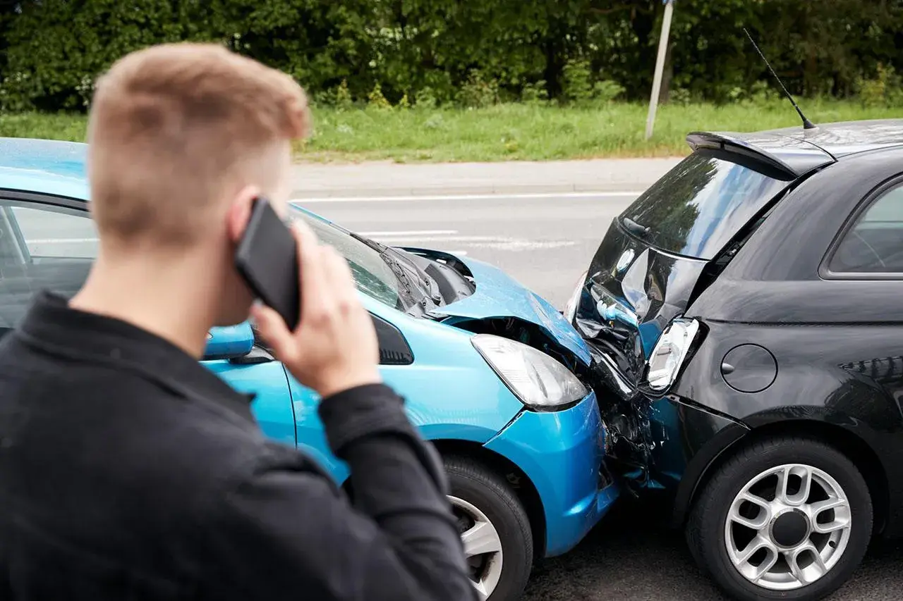 Uomo al telefono dopo un incidente. Le auto sono danneggiate, un sinistro che richiederà un **scoperto assicurativo**.