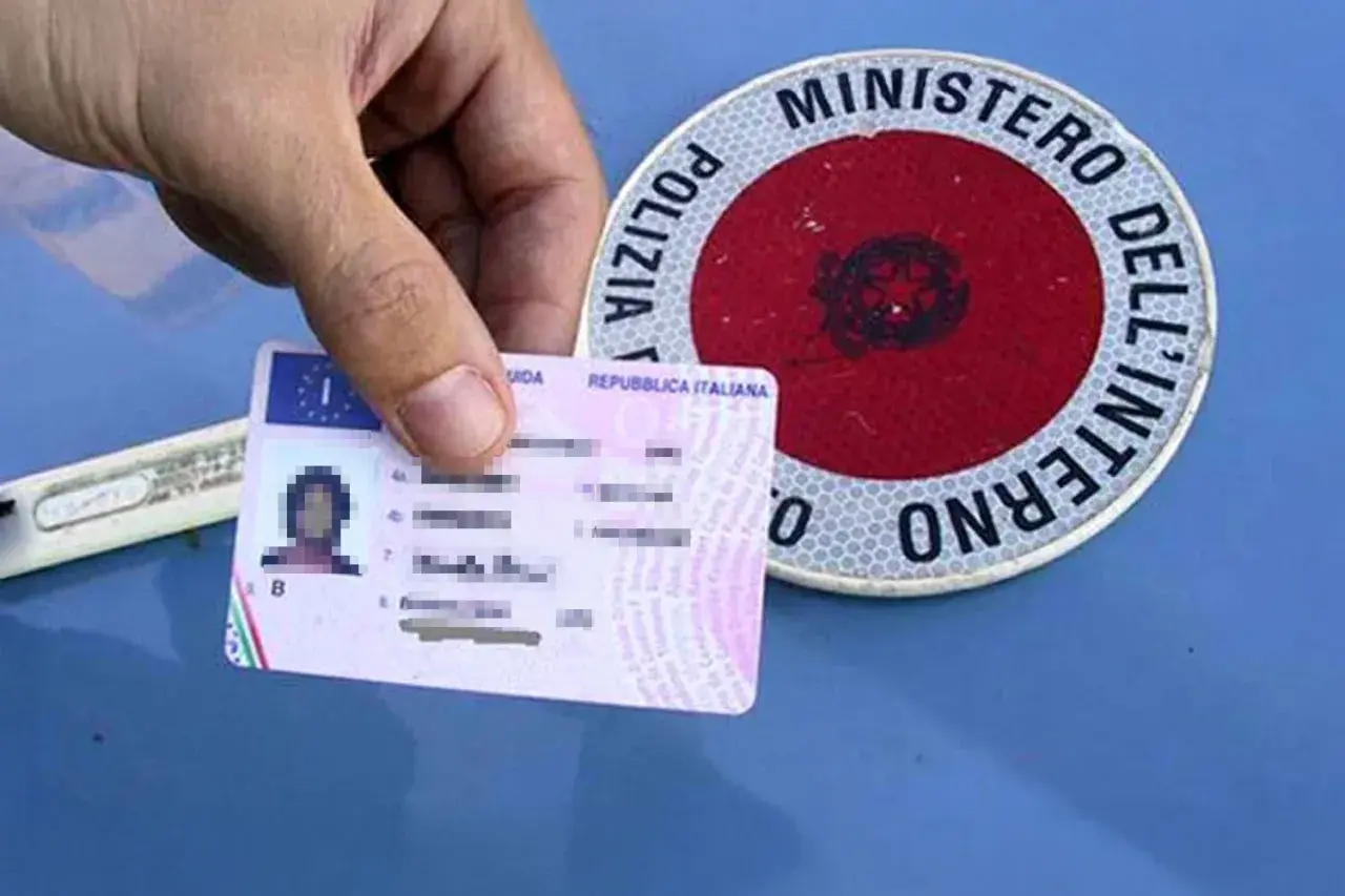 Patente italiana in mano, accanto a un disco di Polizia Stradale. Guida sicura per sapere come recuperare i punti della patente.