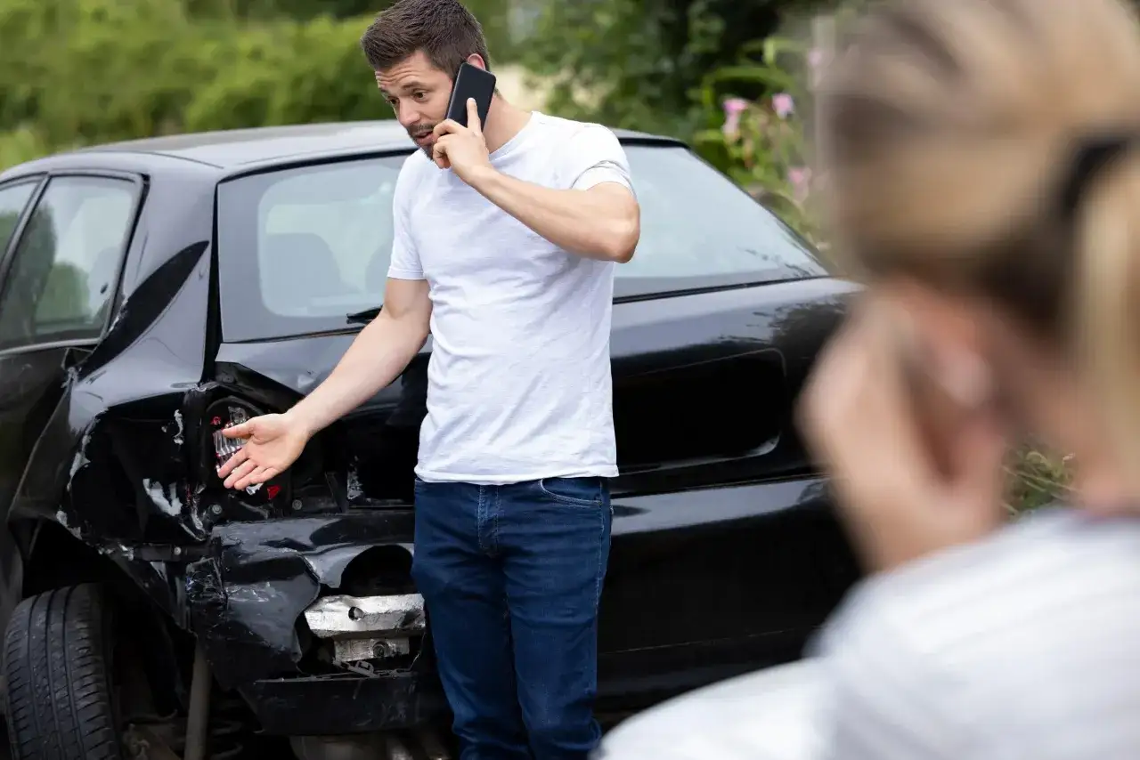 Uomo al telefono mostra l'auto distrutta dopo un incidente. Cosa succede se fai un incidente con il foglio rosa?