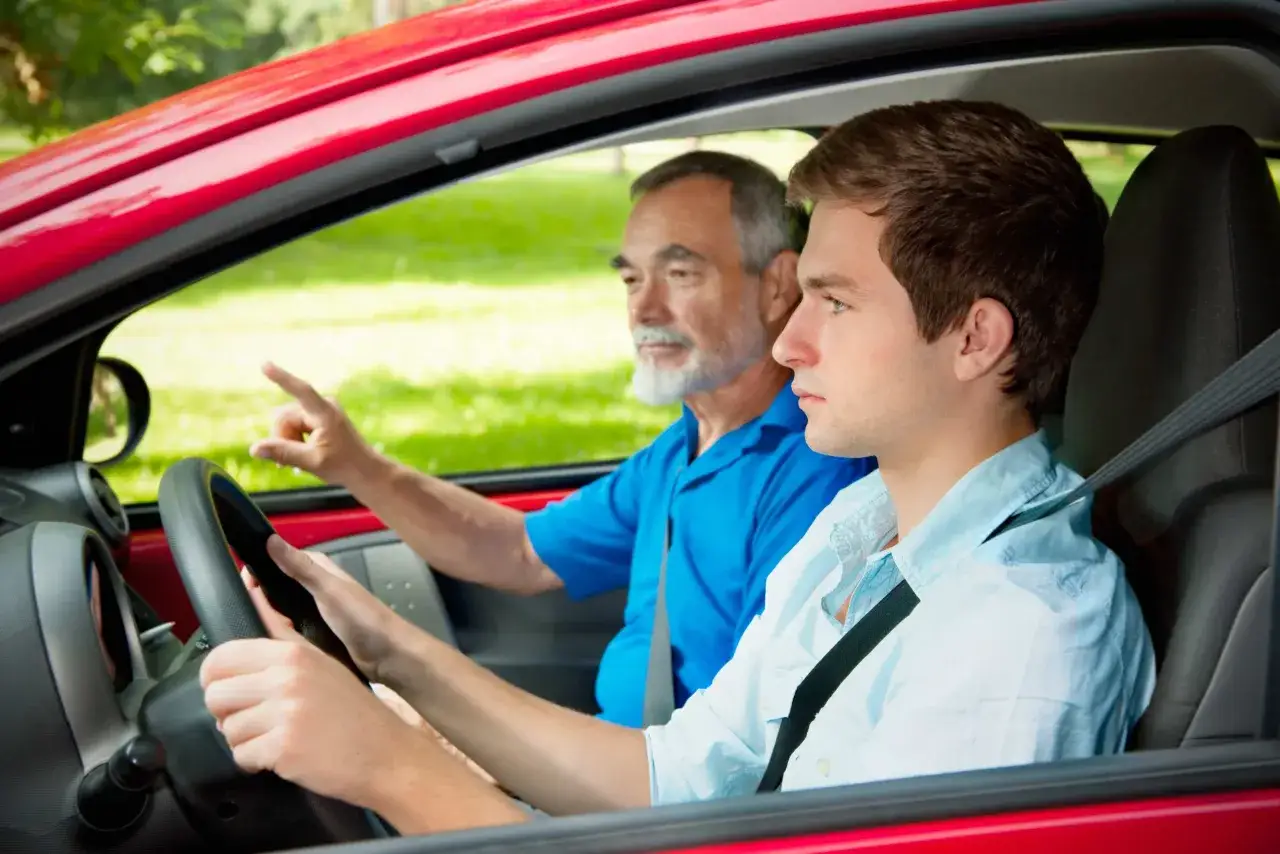Un ragazzo di 17 anni impara a guidare con un adulto che indica la strada.