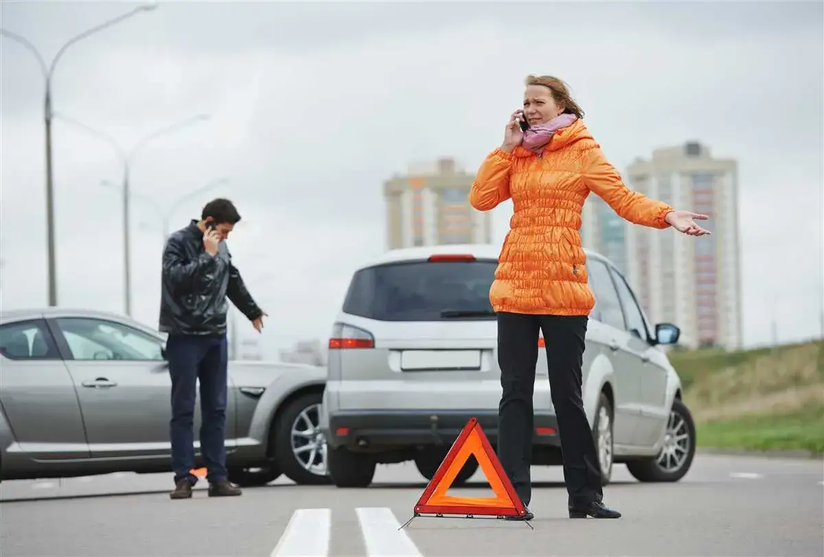Due persone parlano al telefono dopo un incidente stradale, con un triangolo di emergenza posizionato. Ecco cosa fare in caso di incidente.
