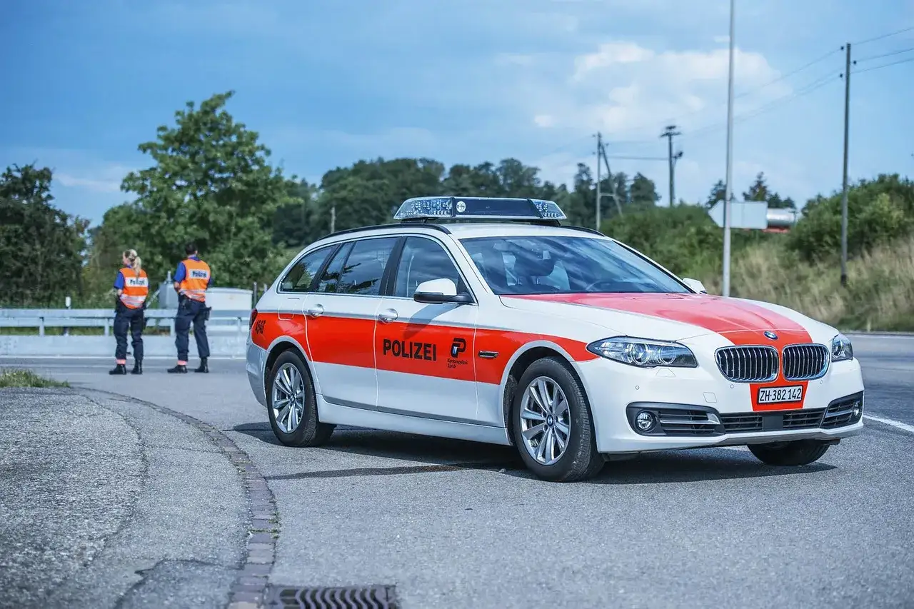 Auto della polizia svizzera ferma sul ciglio della strada, con due agenti in alta visibilità. Forse un controllo per guida senza patente.