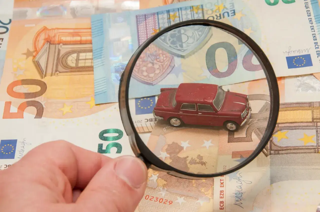 Lente d'ingrandimento su un modellino d'auto e banconote euro, per indagare su una possibile truffa assicurazioni.