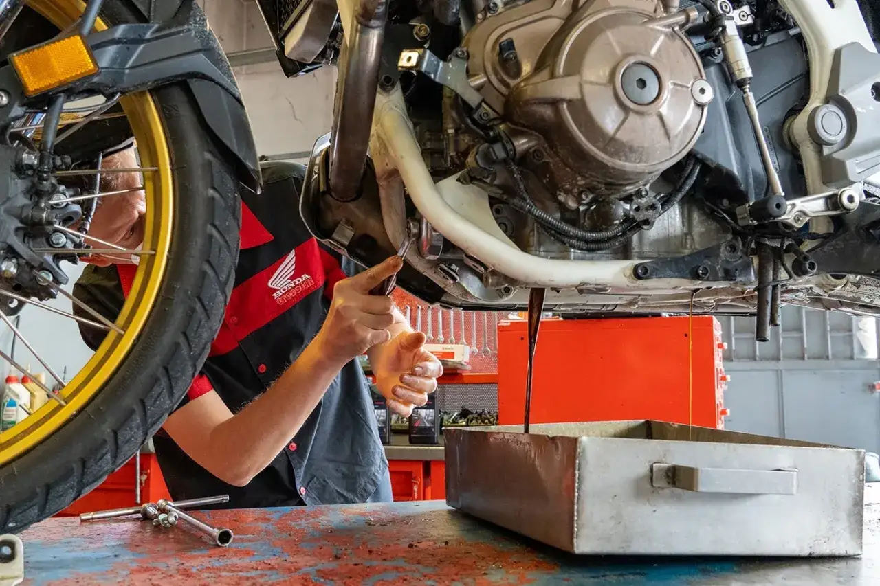 Meccanico esegue il primo tagliando moto, cambiando l'olio motore.