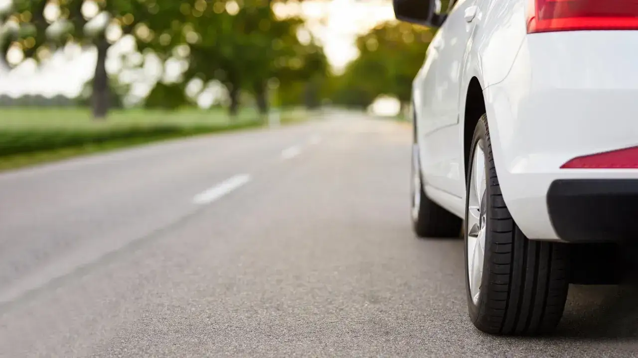 Auto bianca su strada asfaltata, con alberi sullo sfondo. Guida efficiente per il risparmio carburante.