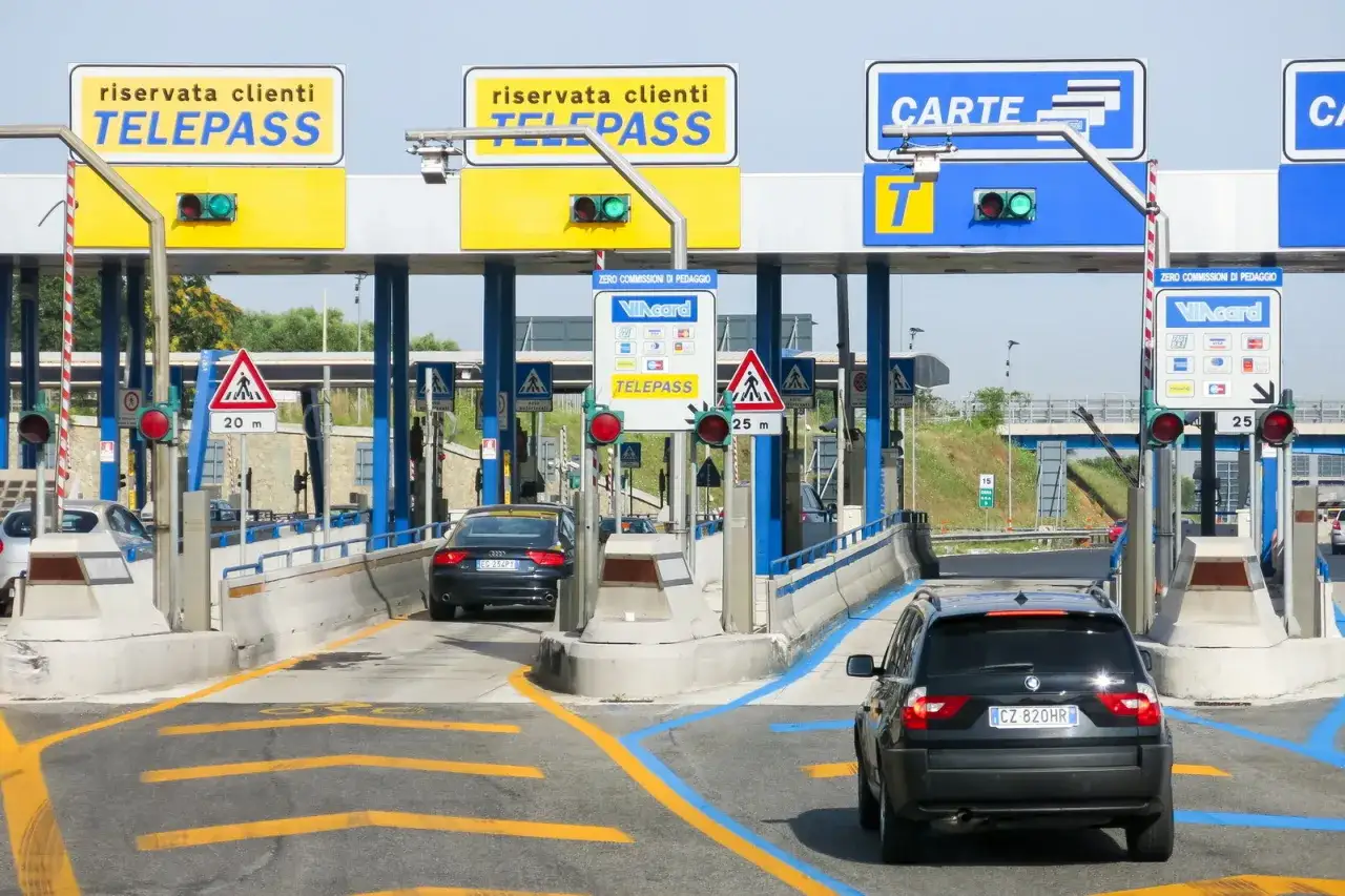 Al casello autostradale, un'auto nera passa sotto i cartelli Telepass. Ecco come funziona Telepass: si avvicina, il semaforo diventa verde e si prosegue.