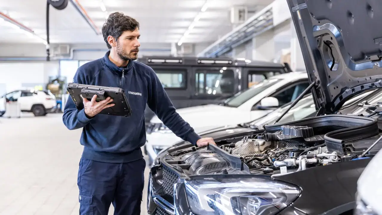 Meccanico con tablet controlla il motore di un'auto. Capire cos'è il tagliando della macchina è fondamentale per la sua manutenzione.