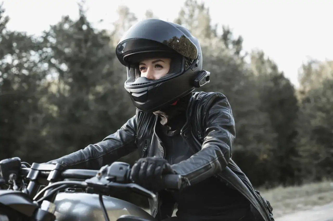 Donna con casco nero su uno scooter, giacca di pelle, guanti. Sguardo intenso verso l'orizzonte.