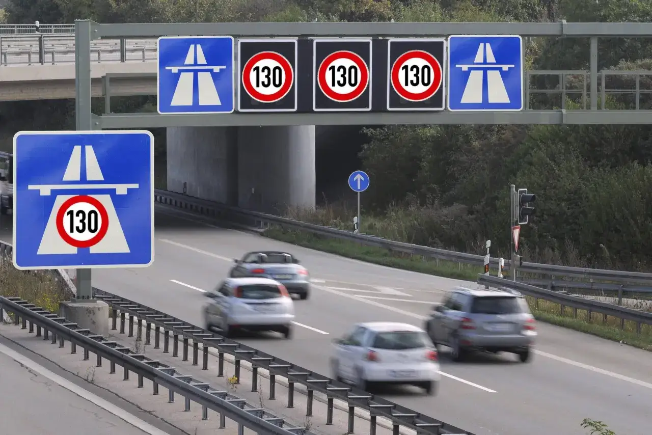 Segnali di limite autostrada 130 km/h, con auto che sfrecciano sull'asfalto bagnato dalla pioggia.