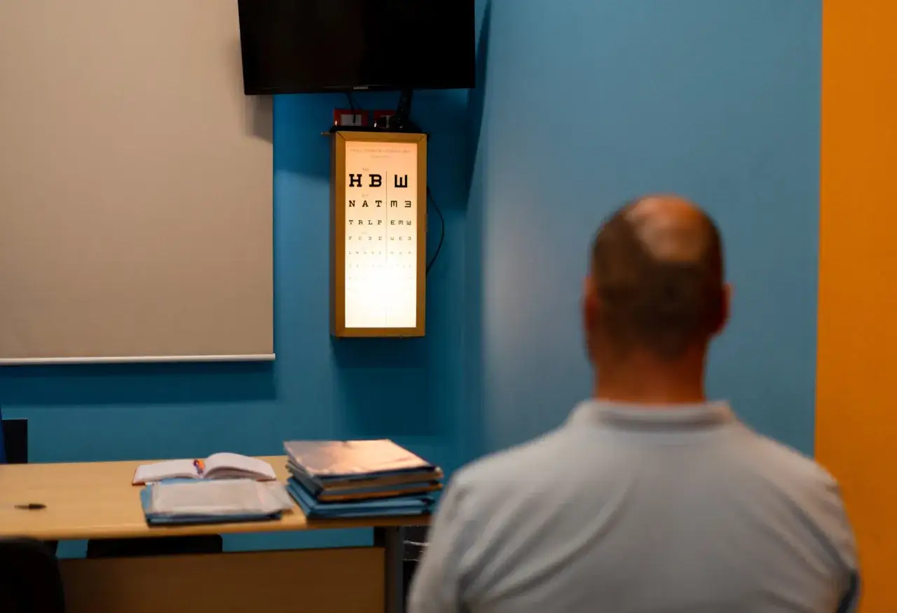 Uomo in visita oculistica per il primo rinnovo patente, con tavola ottometrica illuminata sullo sfondo.