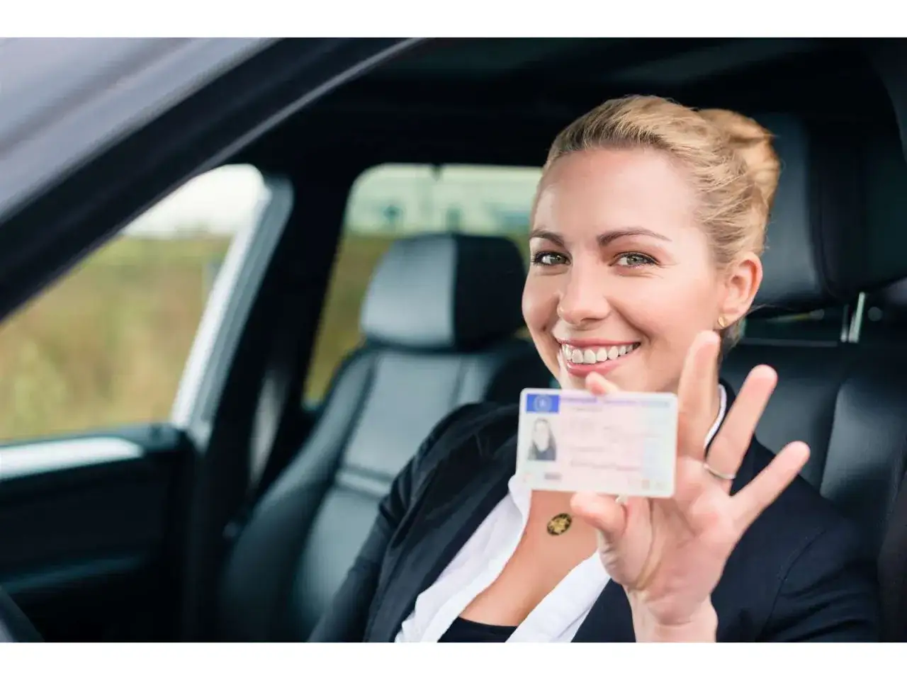 Giovane donna sorride in auto mostrando la patente. Ottima per l'assicurazione auto neopatentati legge Bersani.